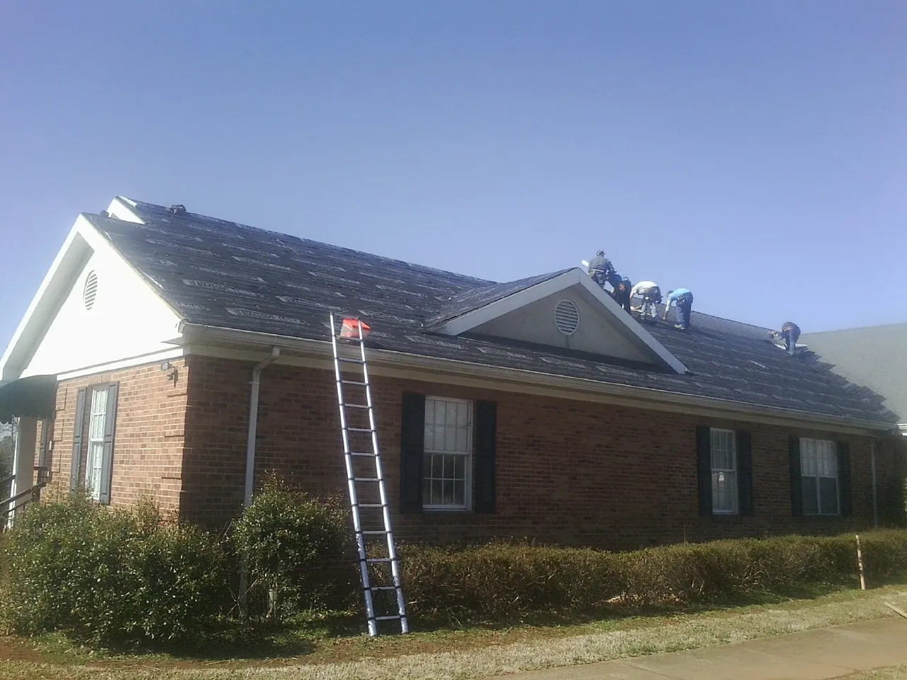 Crew tearing shingles off a brick ranch roof with a ladder set — Metal Roof Repair work by our crew in Otterbein