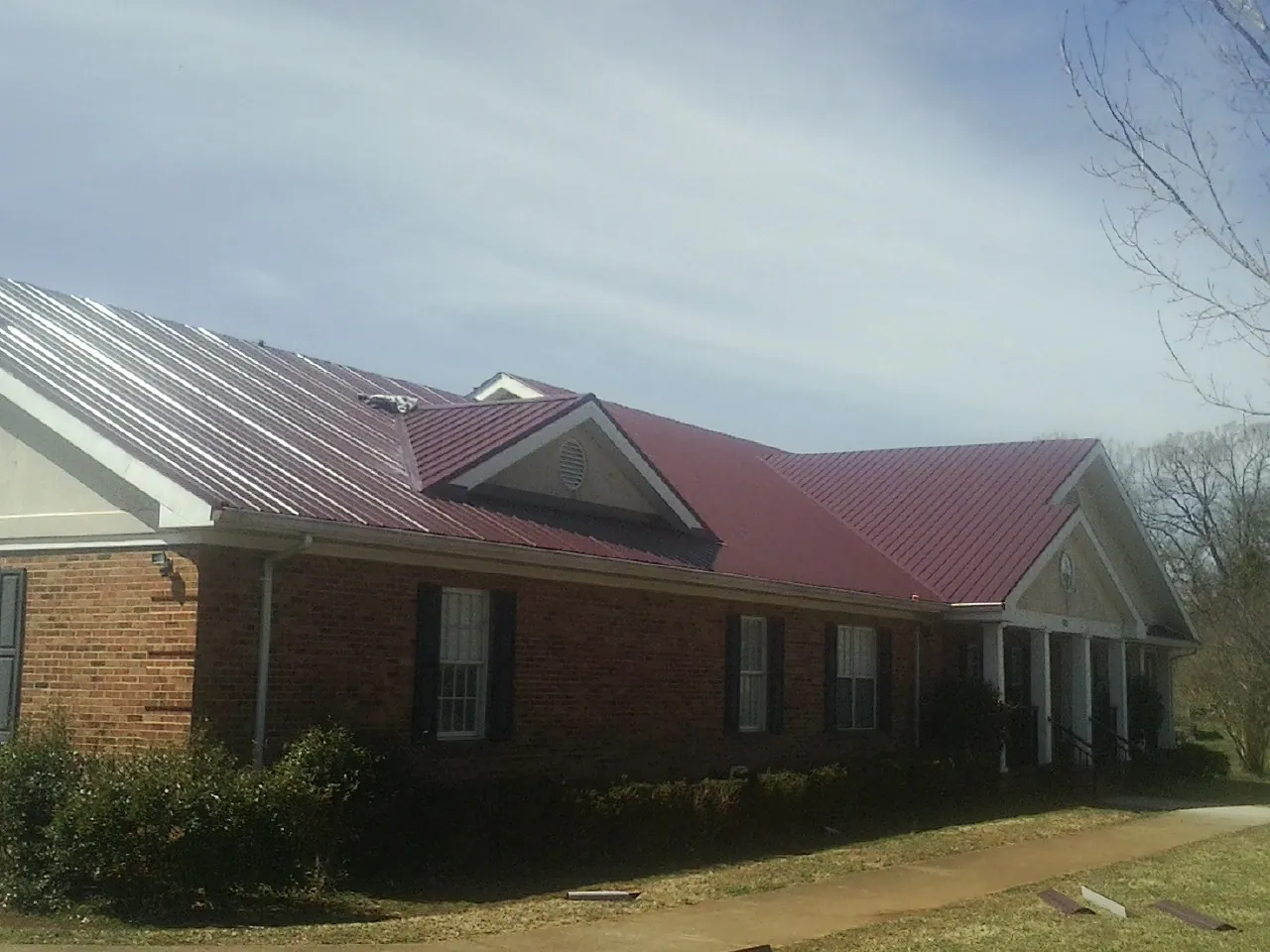 Red metal roof with gabled entries on a long brick building, from a Hail Damage Roof Repair job in Otterbein