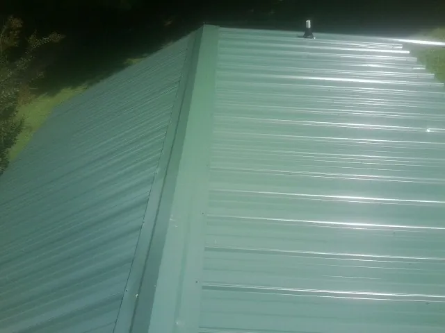 New green metal panels meeting at the ridge of a roof — Flat Roof Repair work by our crew in Otterbein