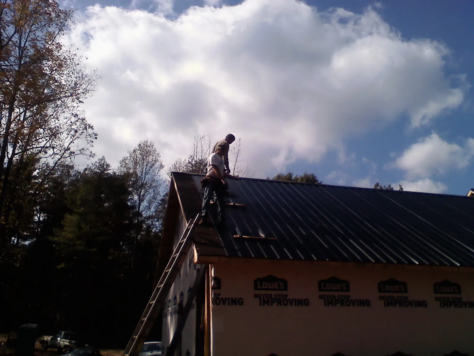 Roofer fastening dark metal panels high against a cloudy sky, from a Roof Inspection job in Otterbein