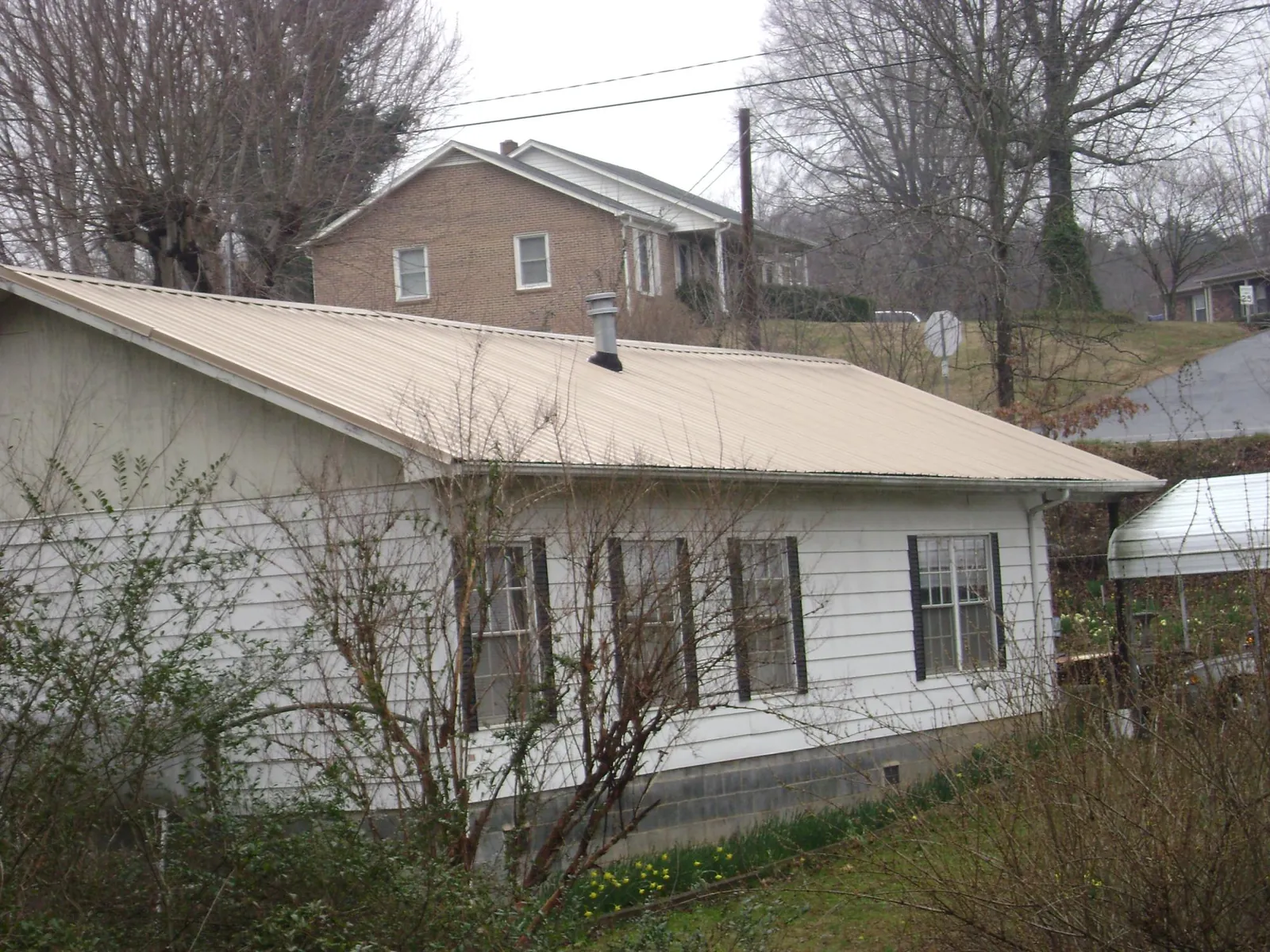 Tan metal roof on a white sided house set into a hillside — Commercial Roofing by Roofing Brothers in Otterbein
